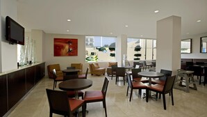 A spacious hotel lobby with multiple seating areas, a flat-screen TV mounted on the wall, and large windows offering a view of the outdoors.