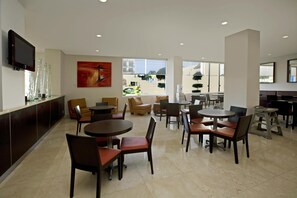 A spacious hotel lobby with multiple seating areas, a flat-screen TV mounted on the wall, and large windows offering a view of the outdoors.
