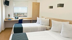 A hotel room with two beds, a desk with a computer, a TV, and a window with a city view.