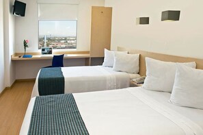 A hotel room with two beds, a desk with a computer, a TV, and a window with a city view.