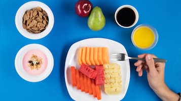 Une assiette contenant des carottes en tranches, de l’ananas et de la pastèque, un bol de céréales, une poire, une pomme et une tasse de café, le tout sur un fond bleu.