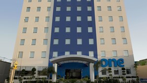 A modern hotel with a prominent 'one' sign, multiple floors, and a landscaped entrance.