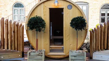 Een houten constructie met een deur, twee potplanten en een klein platform ervoor.