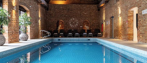 A swimming pool with a tiled edge, surrounded by brick walls and wooden beams.