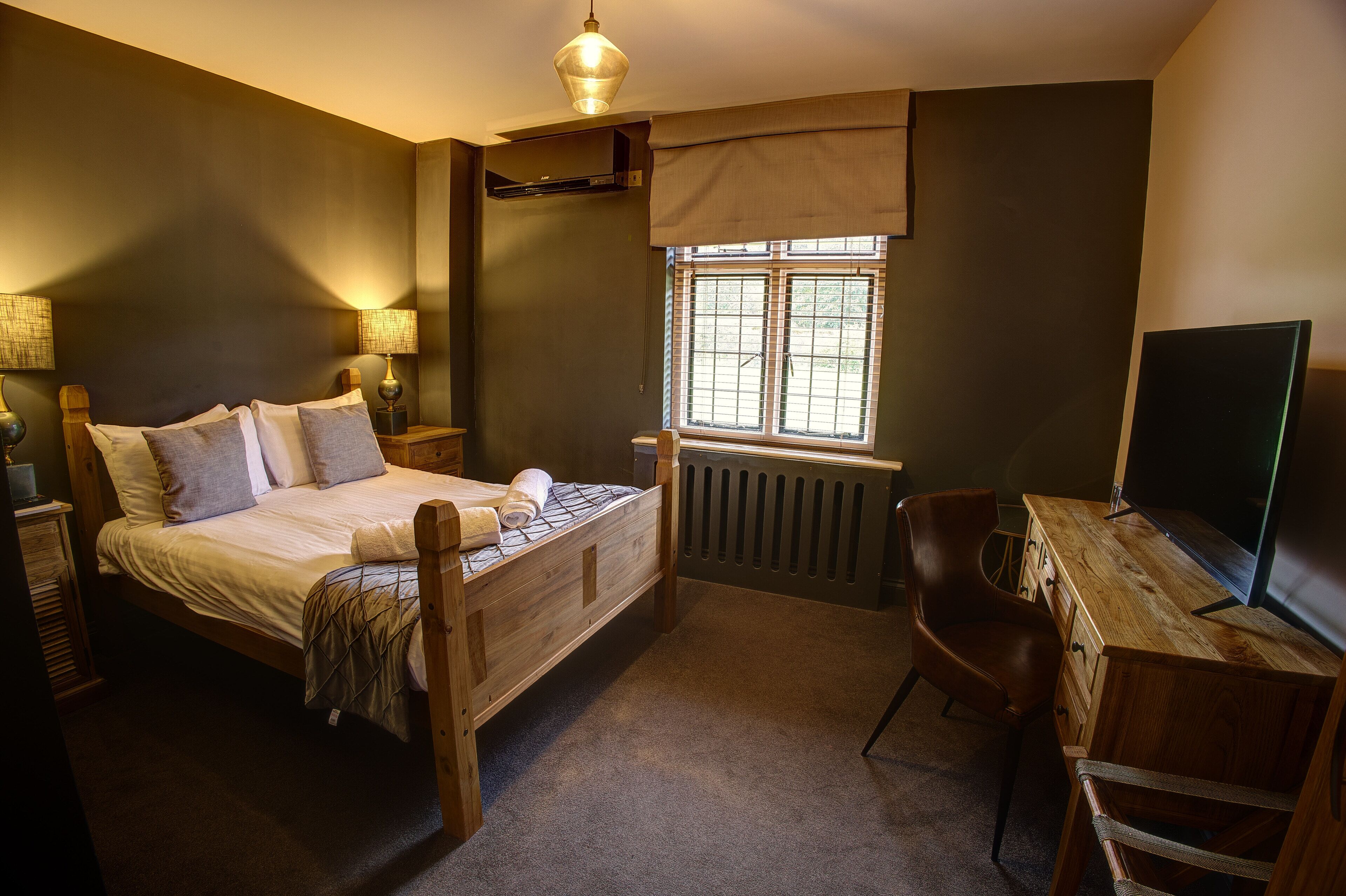 Ein Schlafzimmer mit einem hölzernen Bett, einem Schreibtisch, einem Stuhl, einer Heizung und einem Fenster.
