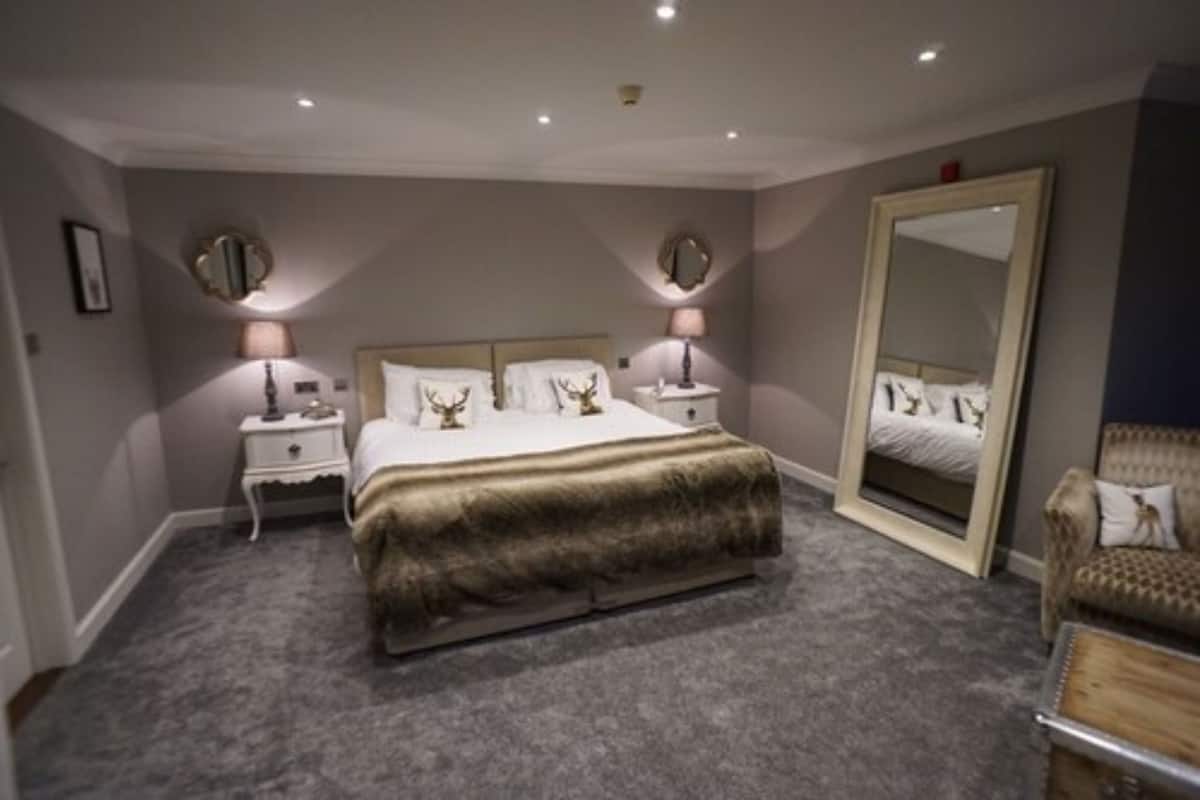 A bedroom with a large bed, two bedside tables with lamps, a large mirror, and a chair.