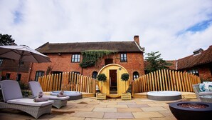 A courtyard with a wooden barrel entrance, lounge chairs, and a hot tub. - Seckford Hall Hotel & Spa (Woodbridge)