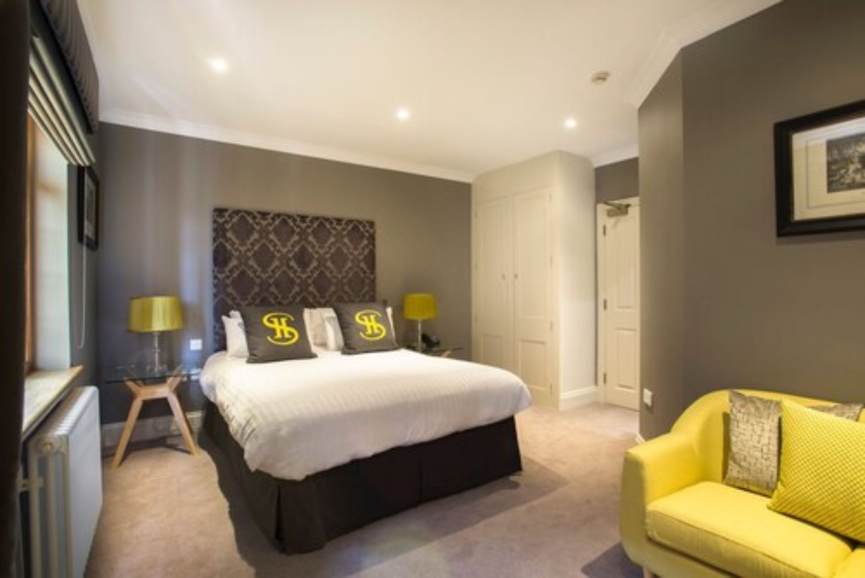 A bedroom with a large bed, two bedside tables with lamps, a yellow sofa, and a wardrobe.