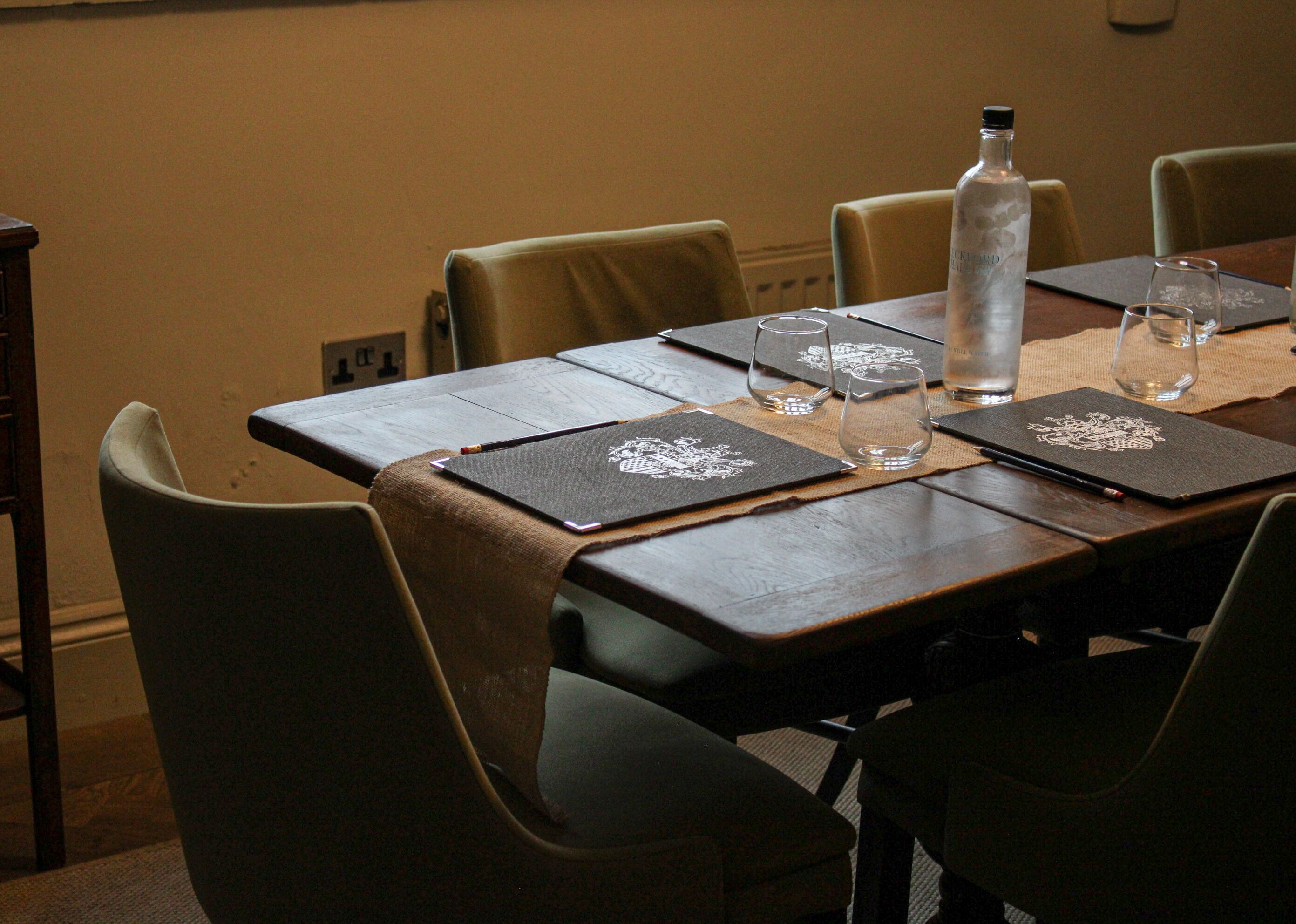 A conference table with a laptop, two glasses, a bottle of water, and a notebook with a crest design.