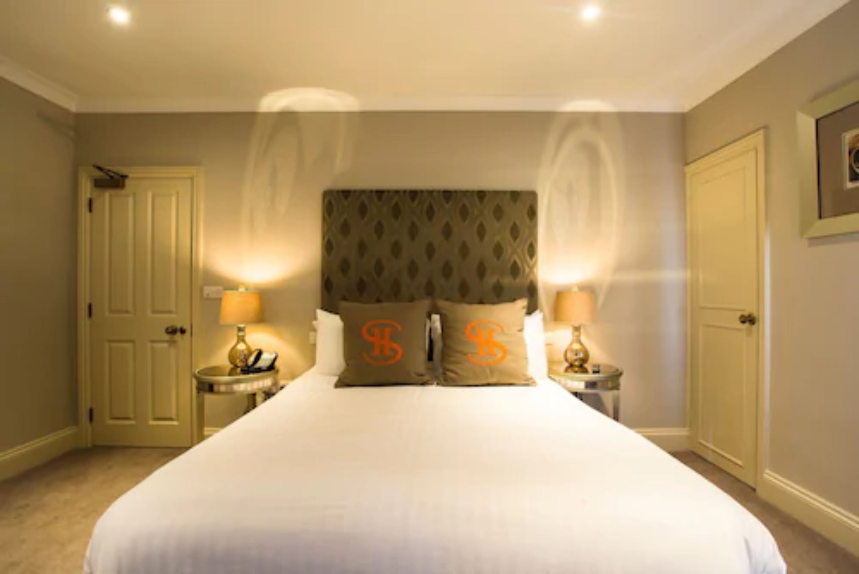 A hotel room with a large bed, two bedside tables with lamps, and a door on the left.