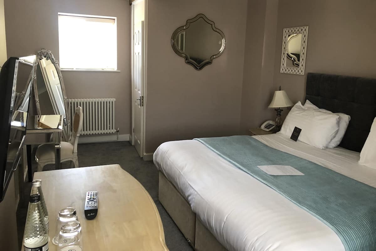 A hotel room with a bed, a bedside table with a remote control, a bottle, and a mirror on the wall.