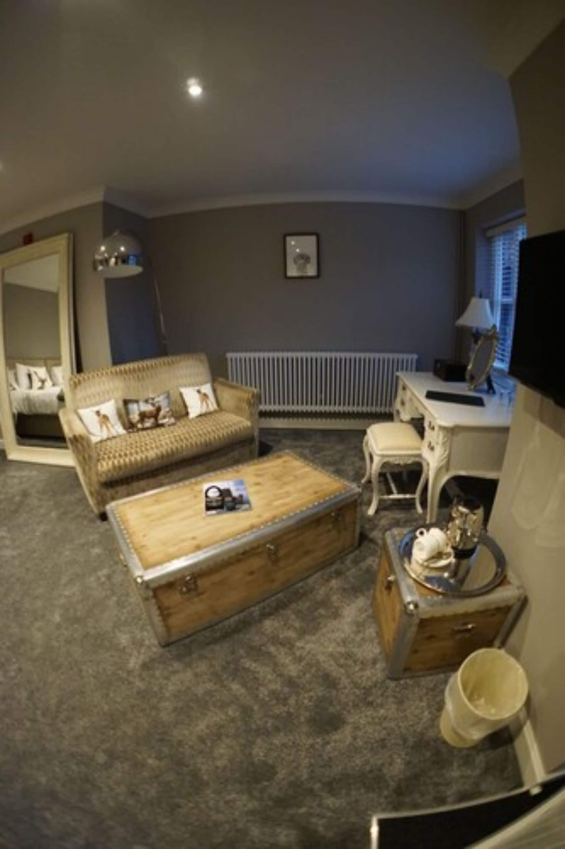 A cozy room with a sofa, a wooden chest, a small table, a mirror, and a radiator.