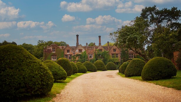 A gravel path leading to a historic building with brick walls and chimneys, surrounded by neatly trimmed hedges. - Seckford Hall Hotel & Spa (Woodbridge)