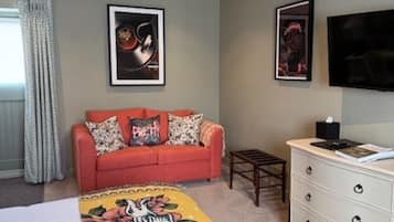 A bedroom with a bed, a sofa, a dresser, and two framed artworks on the wall.