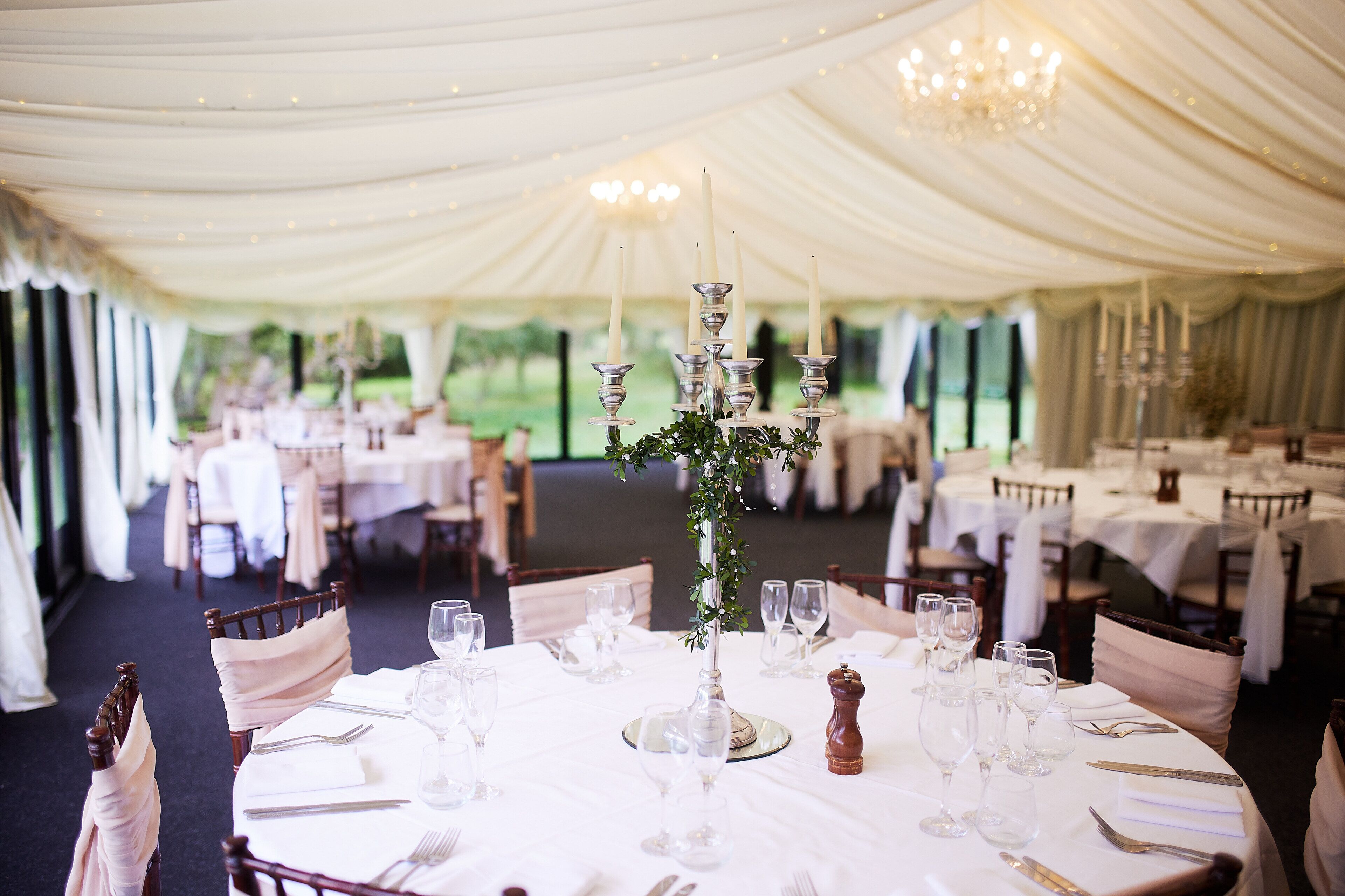 A banquet hall with round tables set for a formal event, featuring white tablecloths, silverware, and glassware.