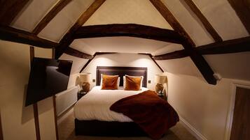 A bedroom with a sloped ceiling, a bed with white bedding and brown pillows, two bedside lamps, and a red throw blanket.