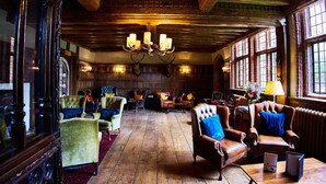 A spacious room with wooden floors, multiple leather armchairs, a chandelier, and large windows. - Seckford Hall Hotel & Spa (Woodbridge)