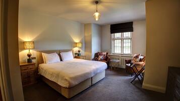 A bedroom with a large bed, two bedside tables with lamps, a chair, a small table, and a window with blinds.