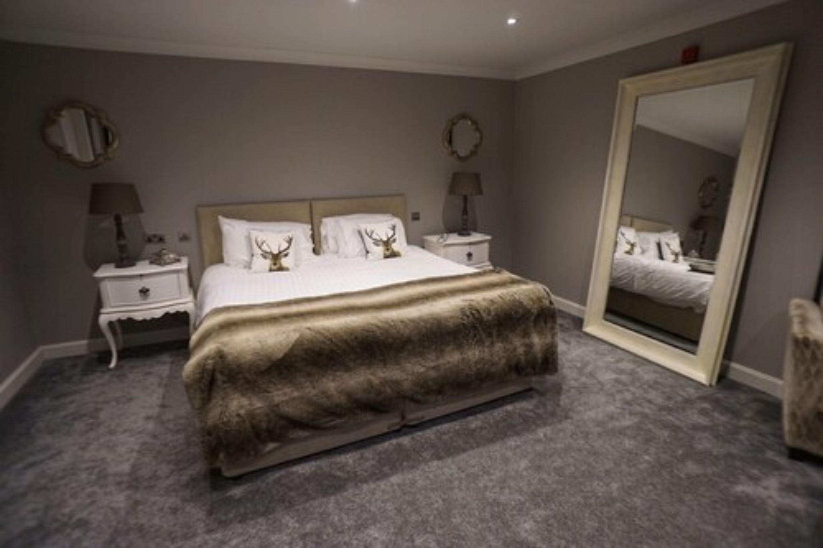 Un dormitorio con una cama grande, dos mesitas de noche, un espejo y piso alfombrado.