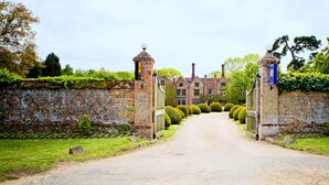 A traditional brick building with a gated entrance, a signboard, and well-maintained hedges. - Seckford Hall Hotel & Spa (Woodbridge)