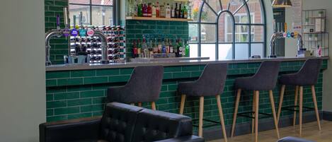 A bar area with stools, a counter with bottles, and a green-tiled wall.