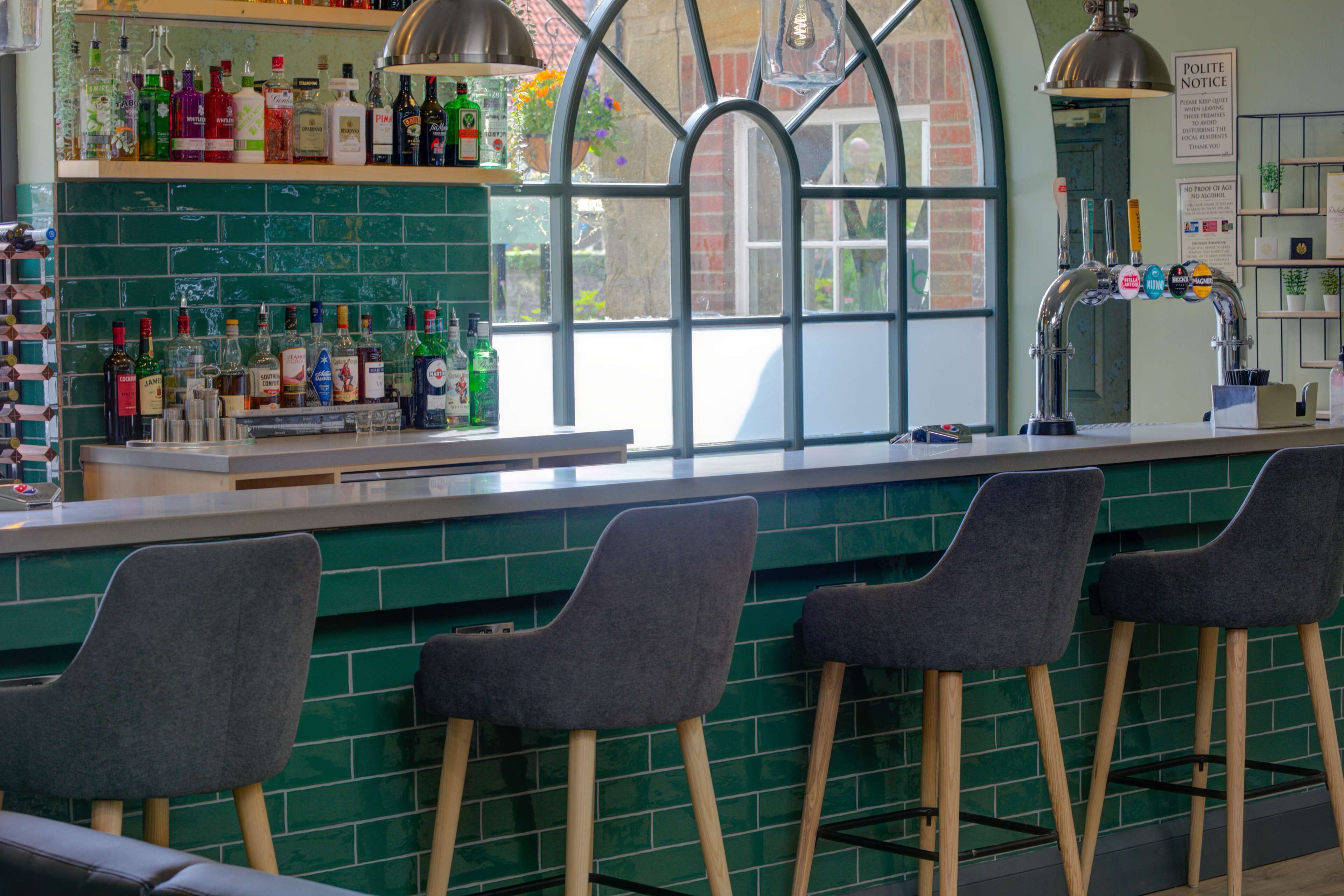 A bar area with green tiled backsplash, a variety of liquor bottles, and bar stools.