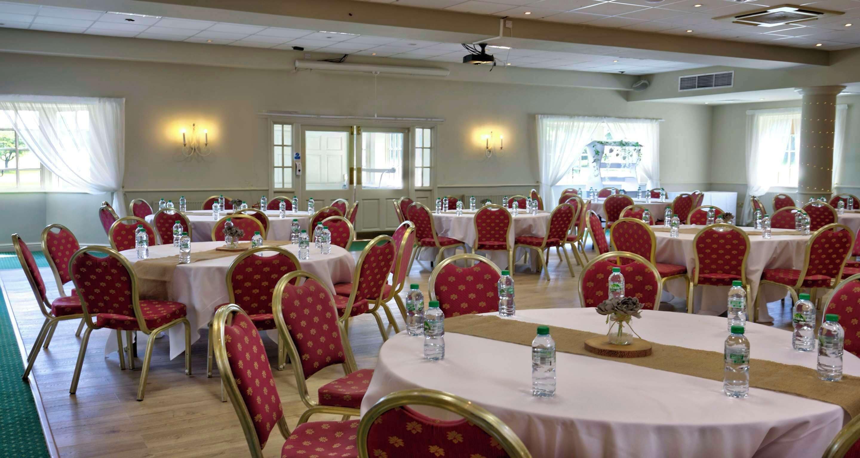 A conference room with round tables, red upholstered chairs, and water bottles on each table.