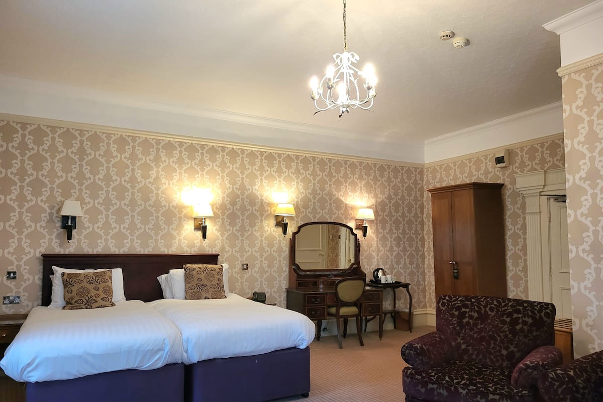 A hotel room with a double bed, two bedside lamps, a dresser, a chair, and a chandelier.