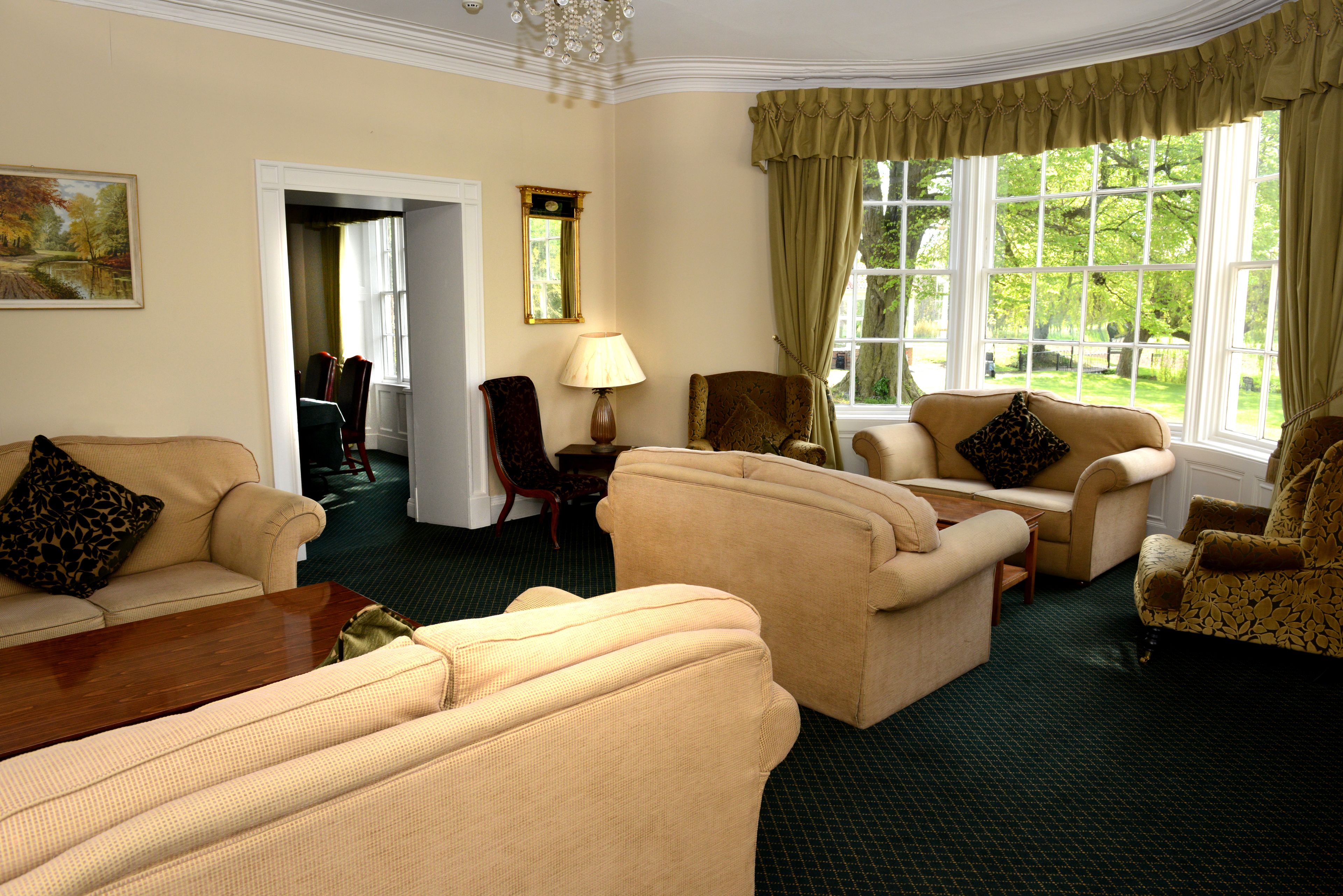 A room with beige sofas, a wooden coffee table, and a view of a garden through large windows.
