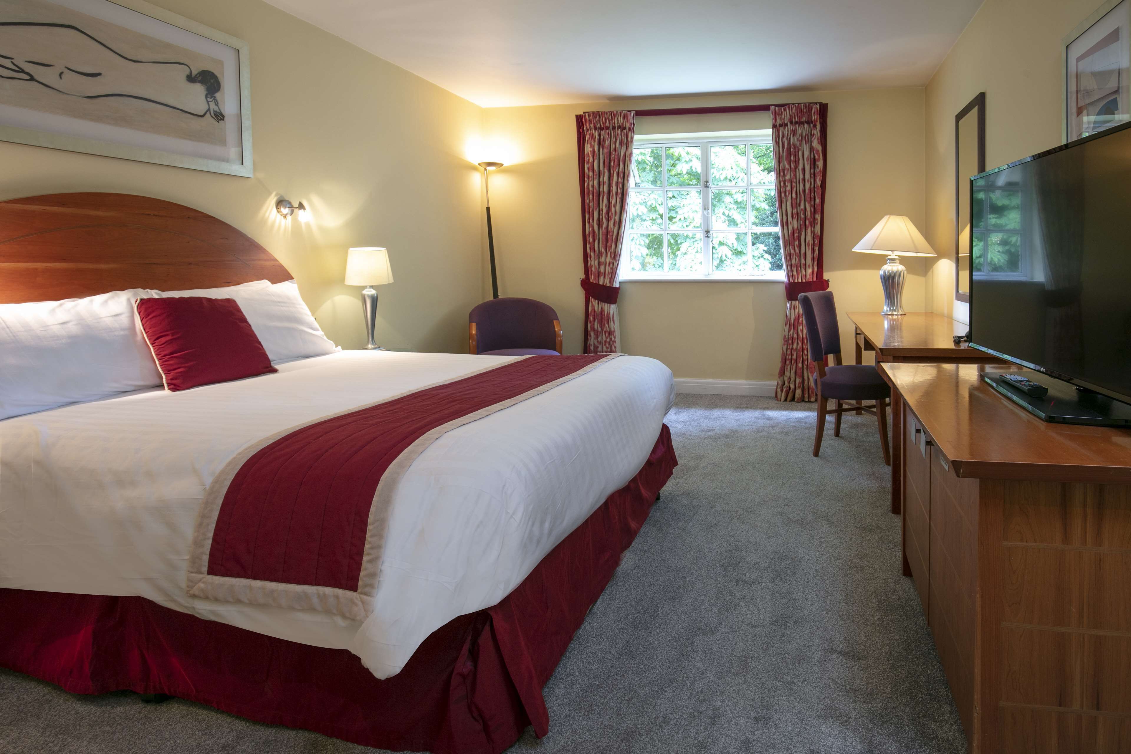 Een hotelkamer met een groot bed, een bureau met een televisie, een stoel en een raam met gordijnen.