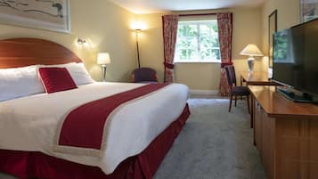 Ein Hotelzimmer mit einem großen Bett, einem Schreibtisch mit Fernseher, einem Sessel und einem Fenster mit Vorhängen.