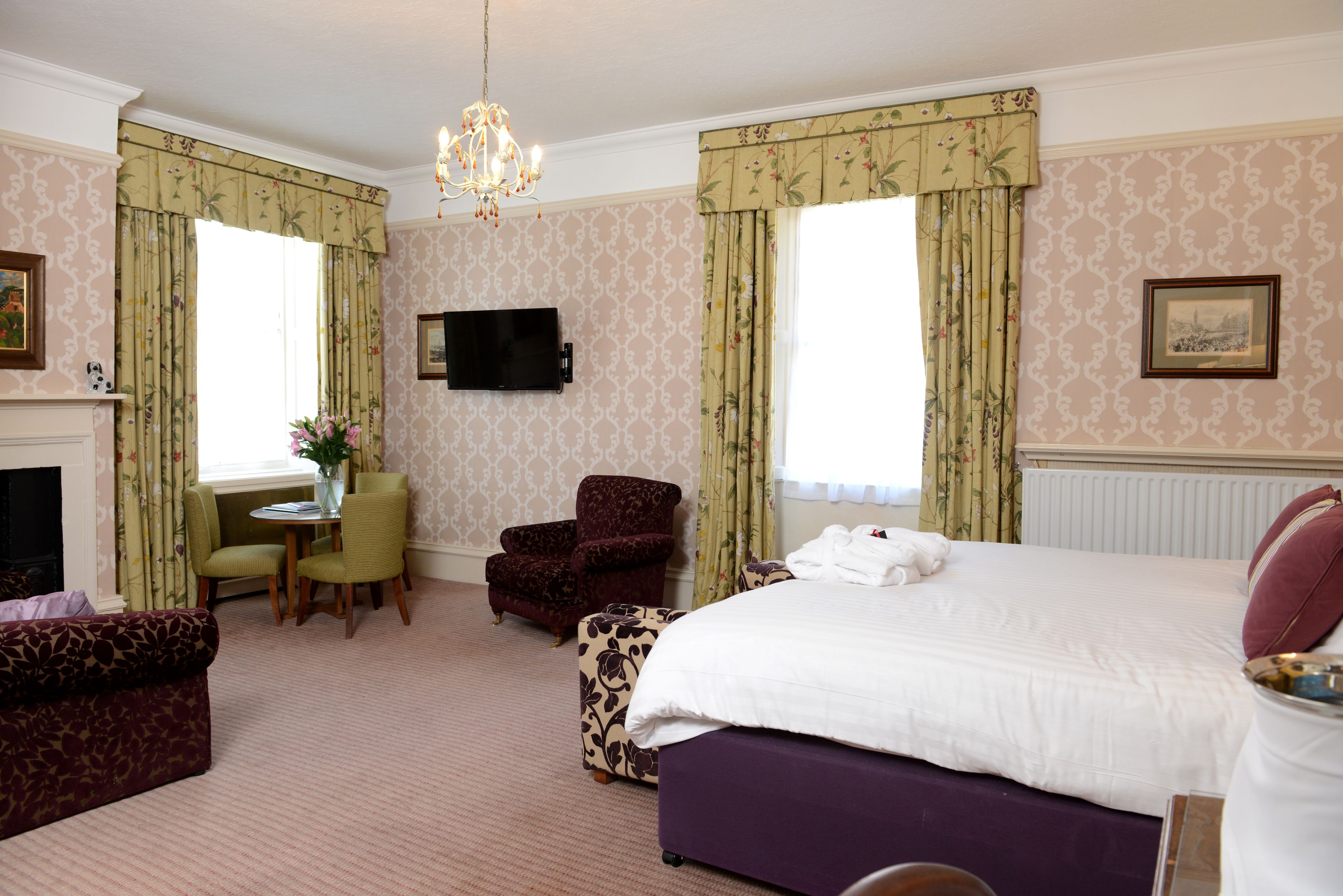A hotel room with a bed, a TV, a fireplace, and a dining area.