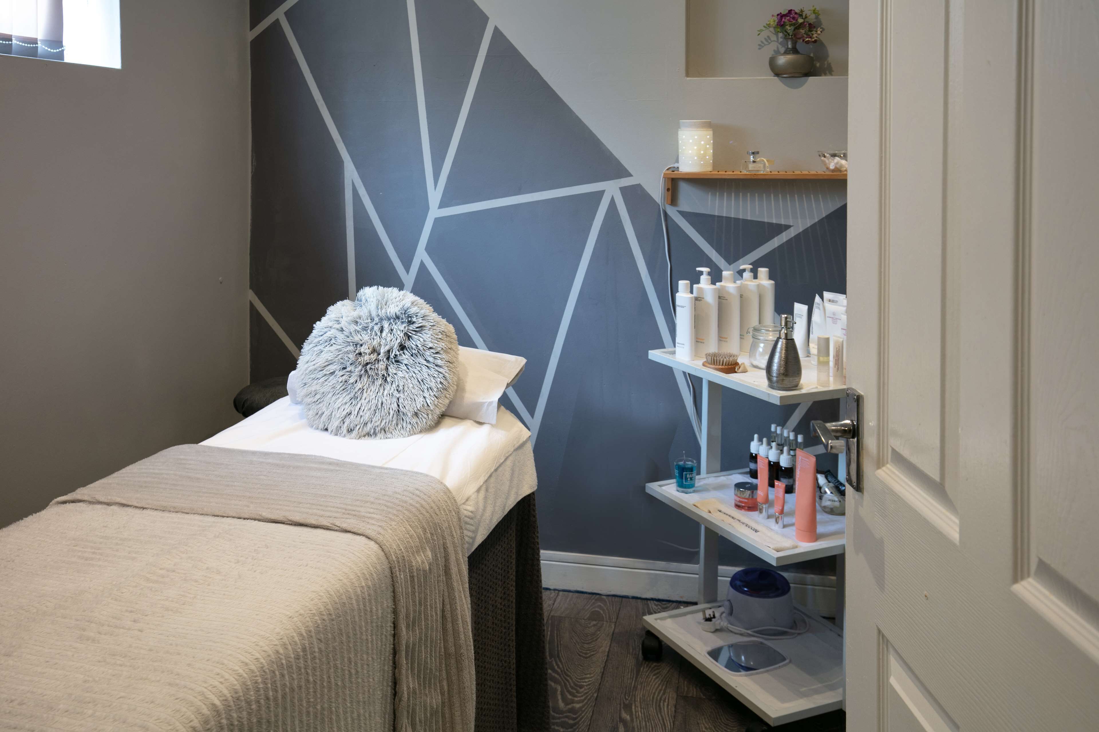 Una habitación ordenada con una cama, un estante con artículos de aseo y un diseño geométrico en la pared.