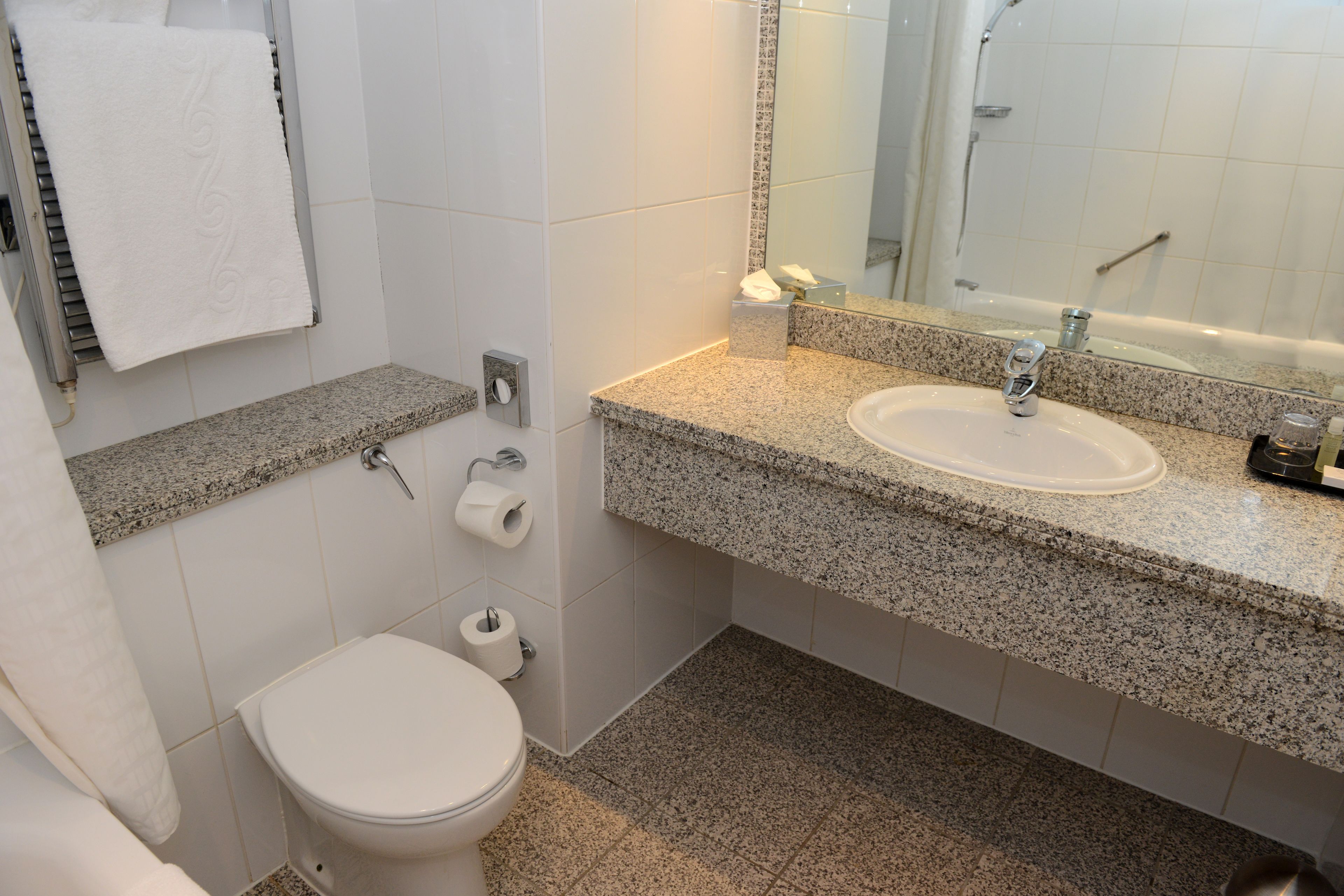 A bathroom with a white toilet, a granite countertop sink, a mirror, and a towel rack.