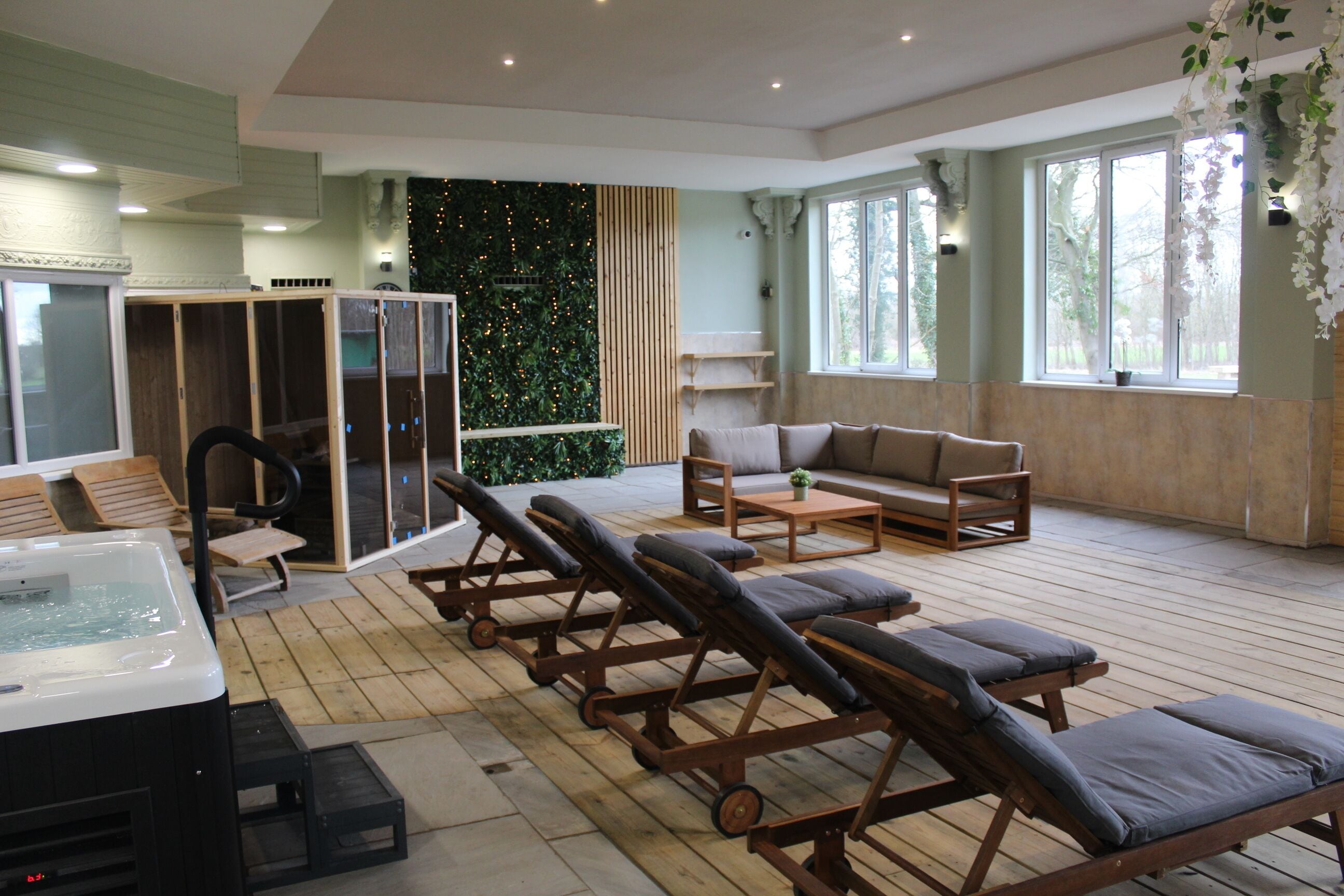 A spa area with a hot tub, sun loungers, a sofa, and a wall with greenery.