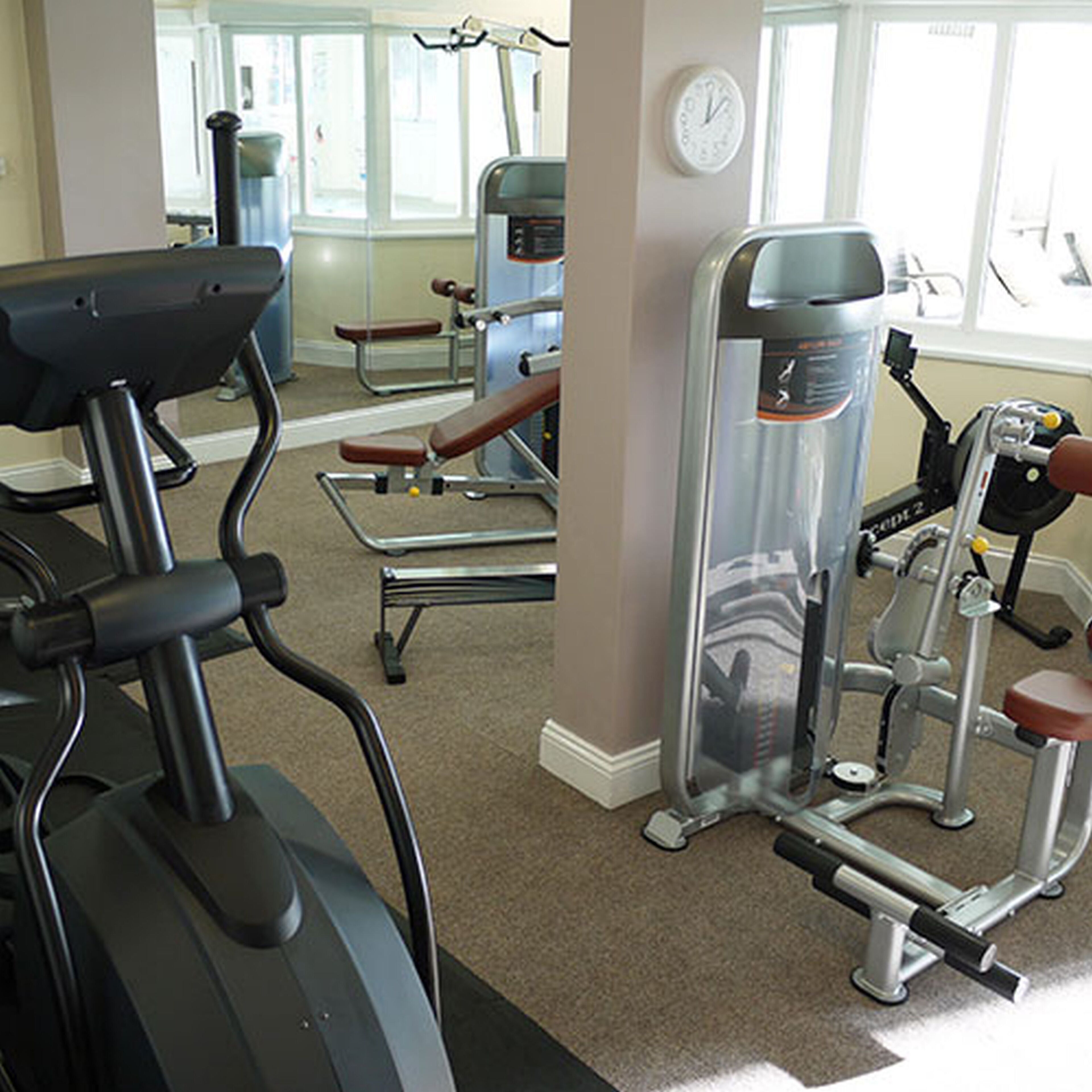 A gym with cardio equipment, weight machines, and a wall clock.
