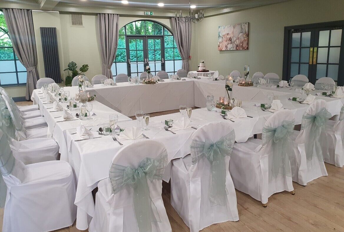A conference room with round tables, white tablecloths, and chairs with light blue sashes.