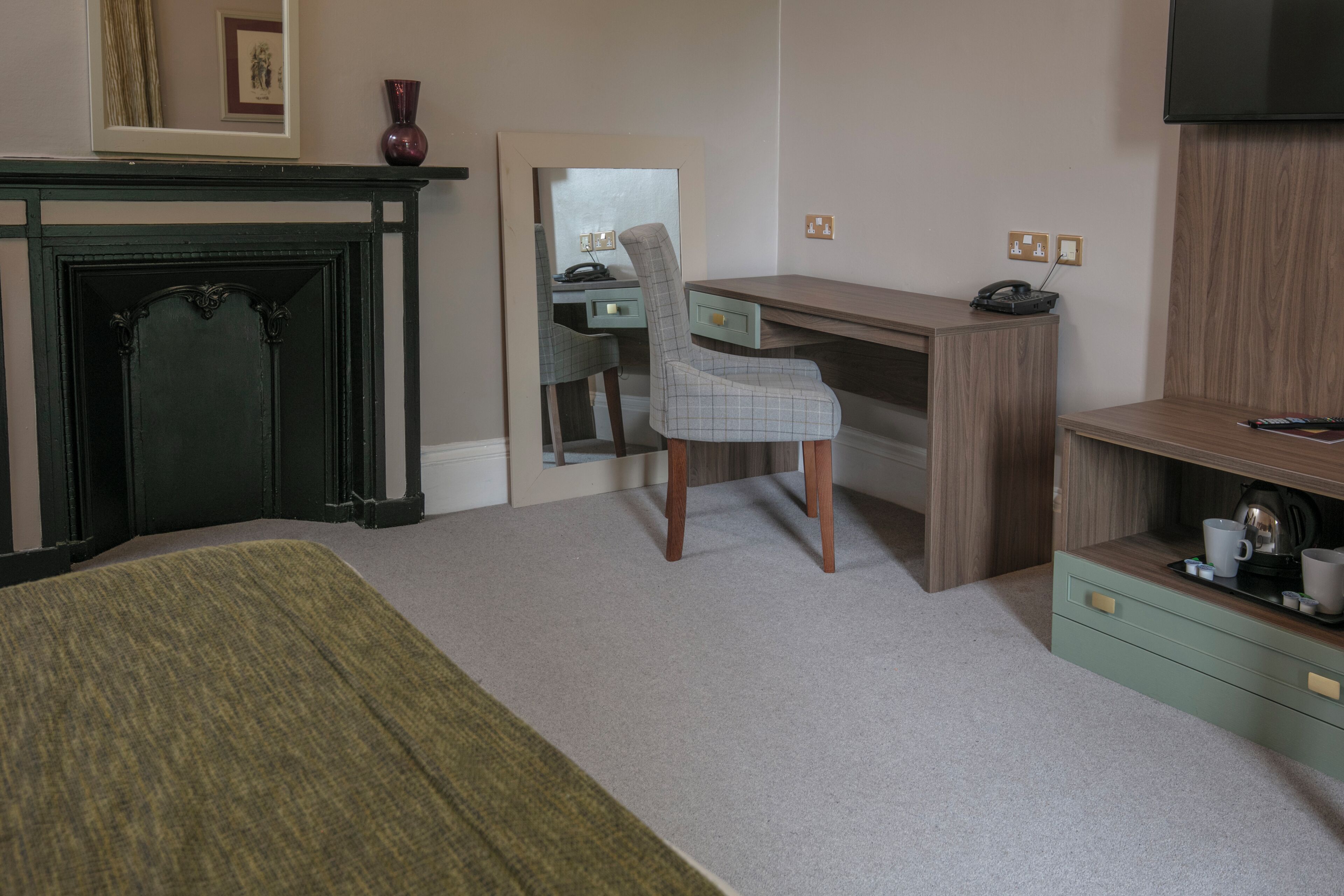 A hotel room with a bed, a desk, a chair, a television, and a fireplace.
