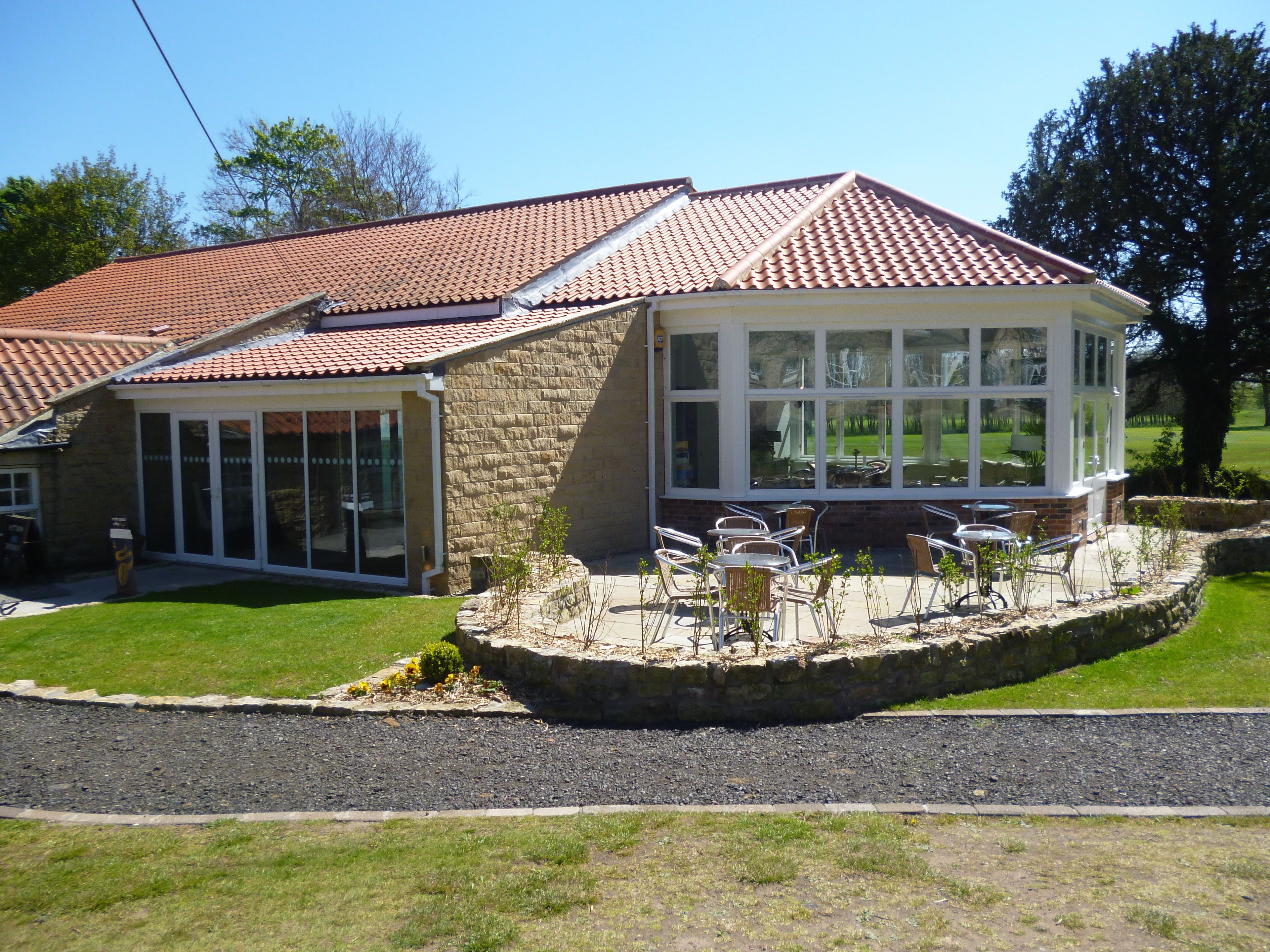 A house with a tiled roof, a covered patio with outdoor furniture, and a stone retaining wall.