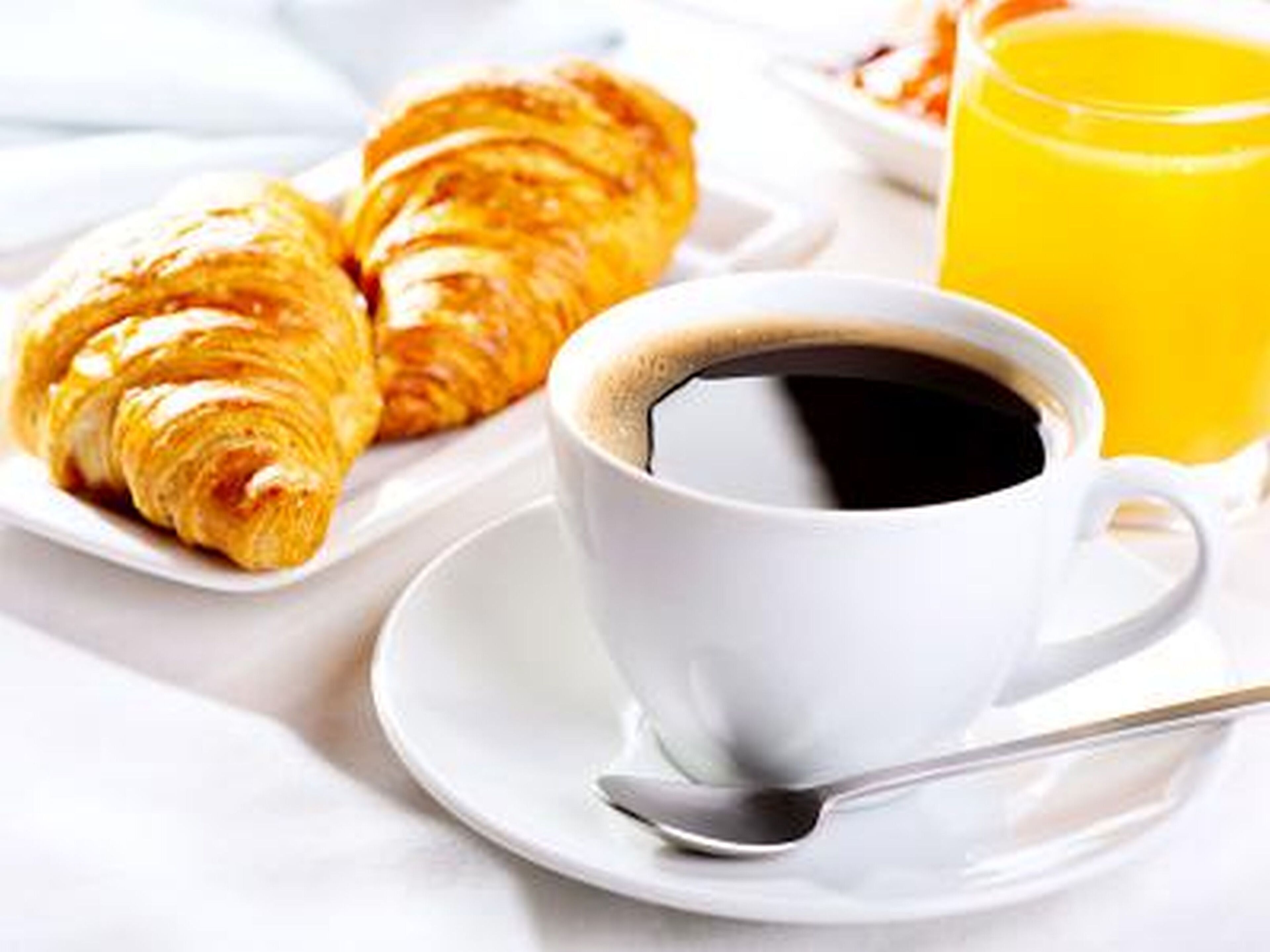 A breakfast setting with croissants, a cup of coffee, and a glass of orange juice.