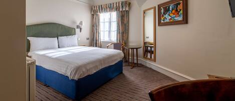 A hotel room with a large bed, a chair, a small table, and a painting on the wall.