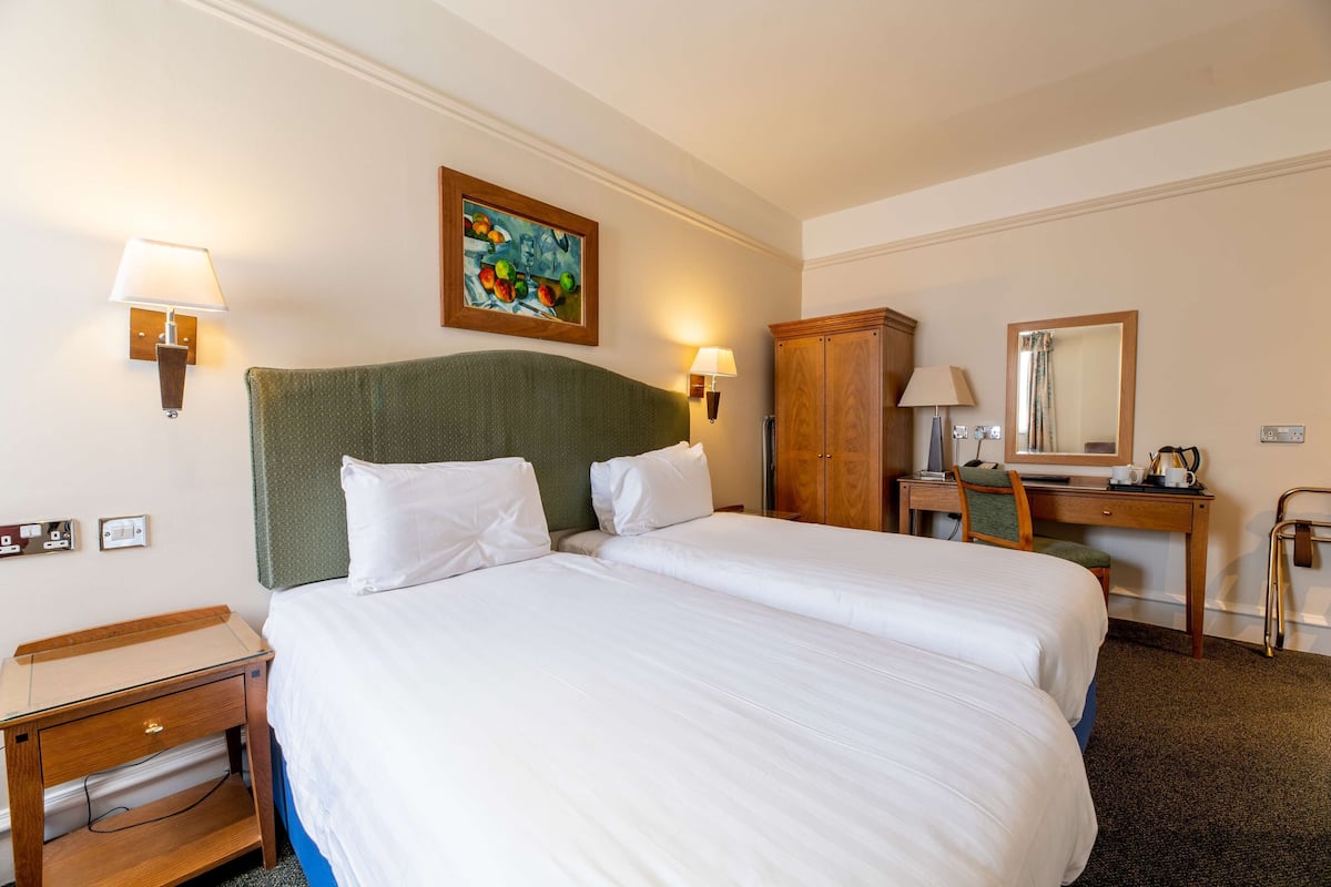 A hotel room with a large bed, two bedside tables, a desk, a chair, a wardrobe, and a painting on the wall.