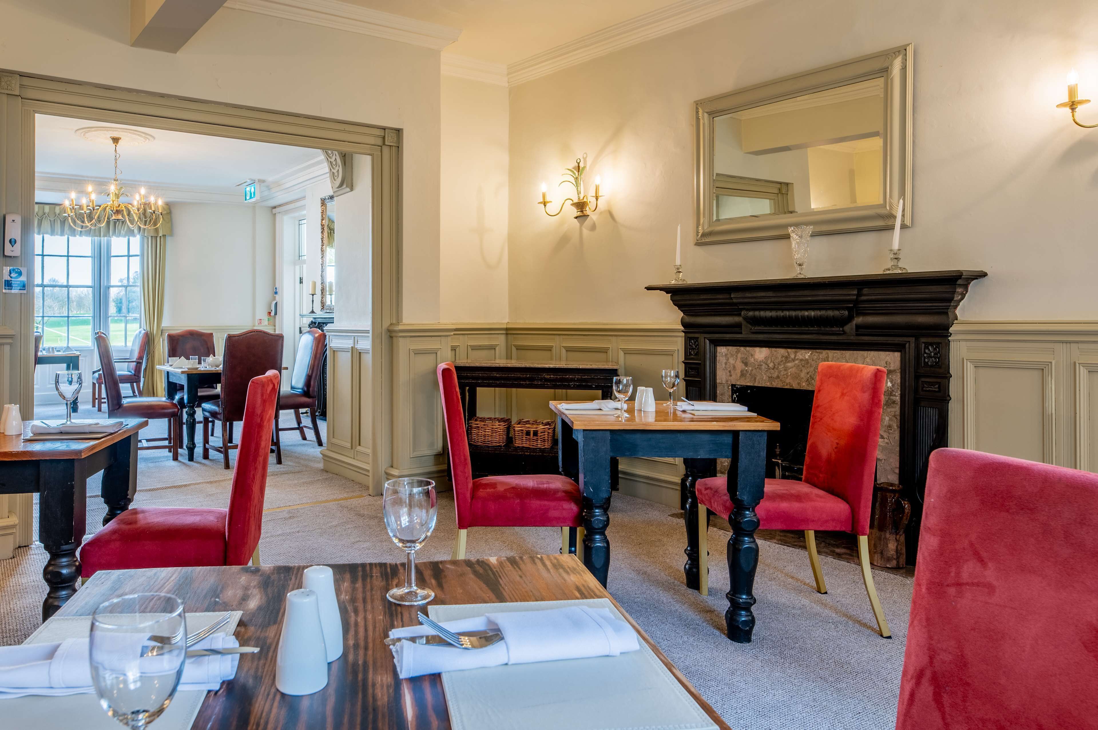 A dining area with red upholstered chairs, wooden tables, and a fireplace.