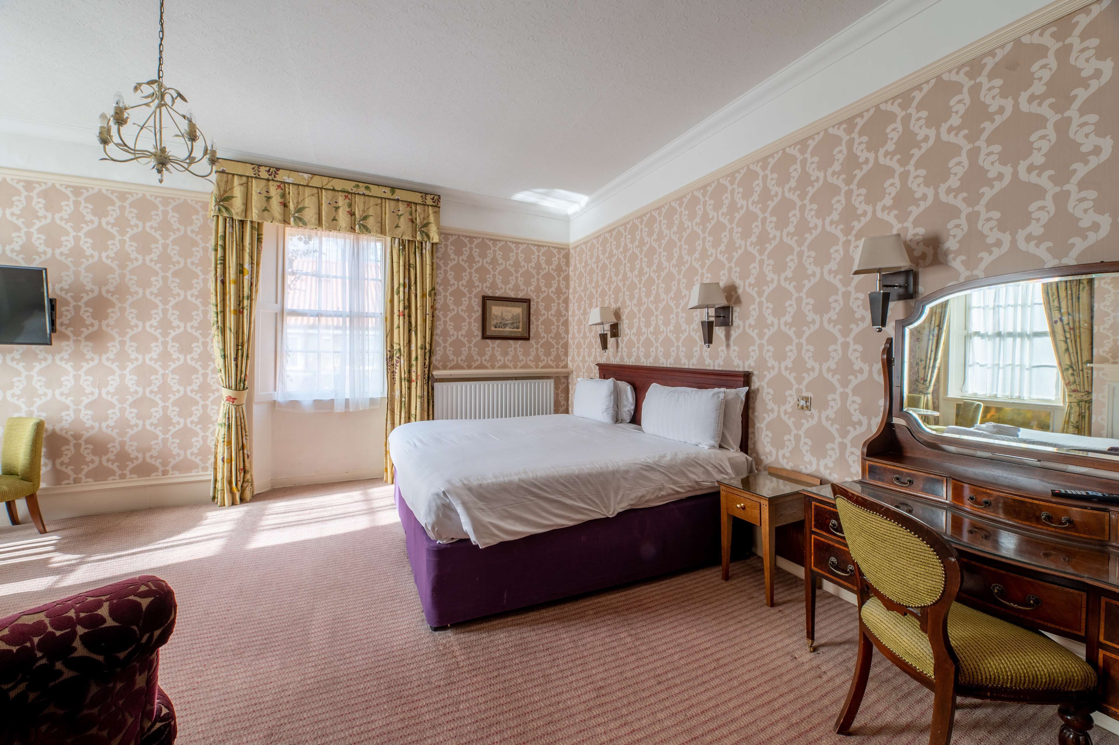 A hotel room with a large bed, a desk with a mirror, a chair, and a television.