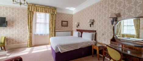 A hotel room with a large bed, a desk with a mirror, a chair, and a television.