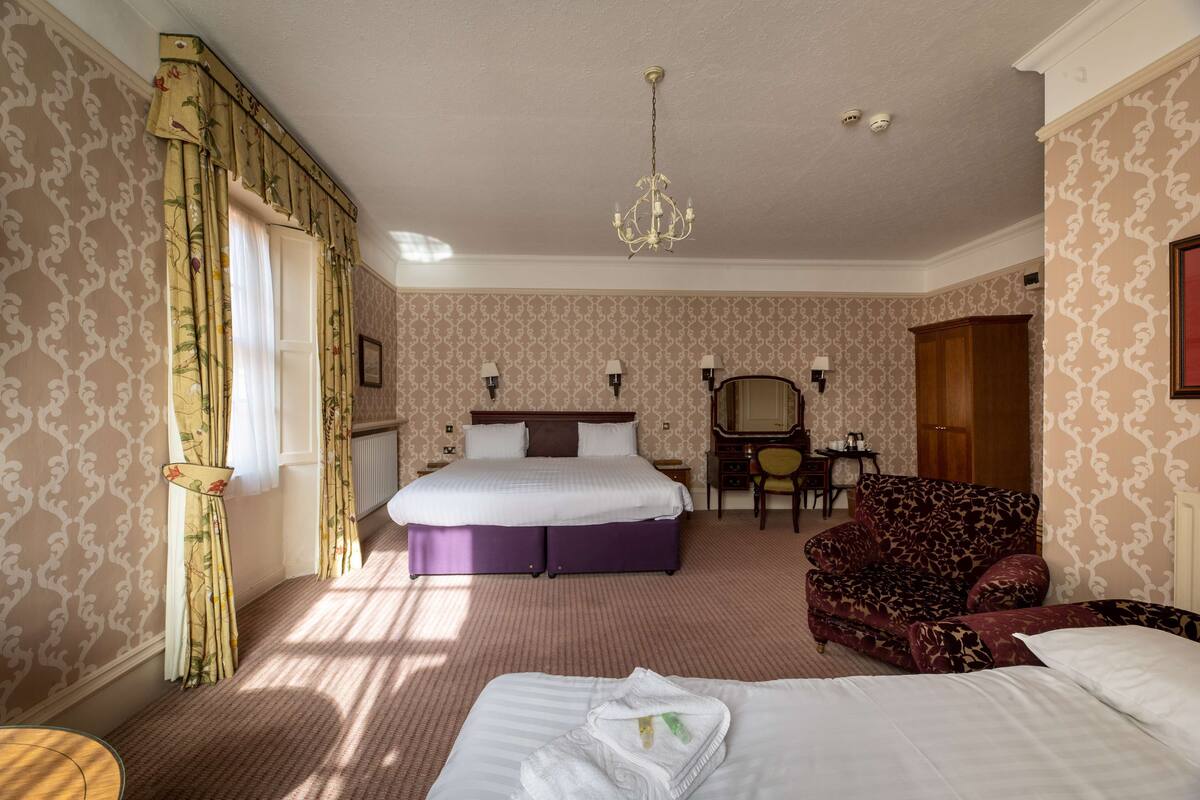 A hotel room with a bed, a chair, a desk, and a chandelier.