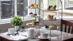 A three-tiered tea service stand with various sandwiches and pastries, a white teapot, cups, and a small potted plant on a table by a window. - Hall Garth Hotel Darlington, Sure Hotel Collection by BW (Darlington)