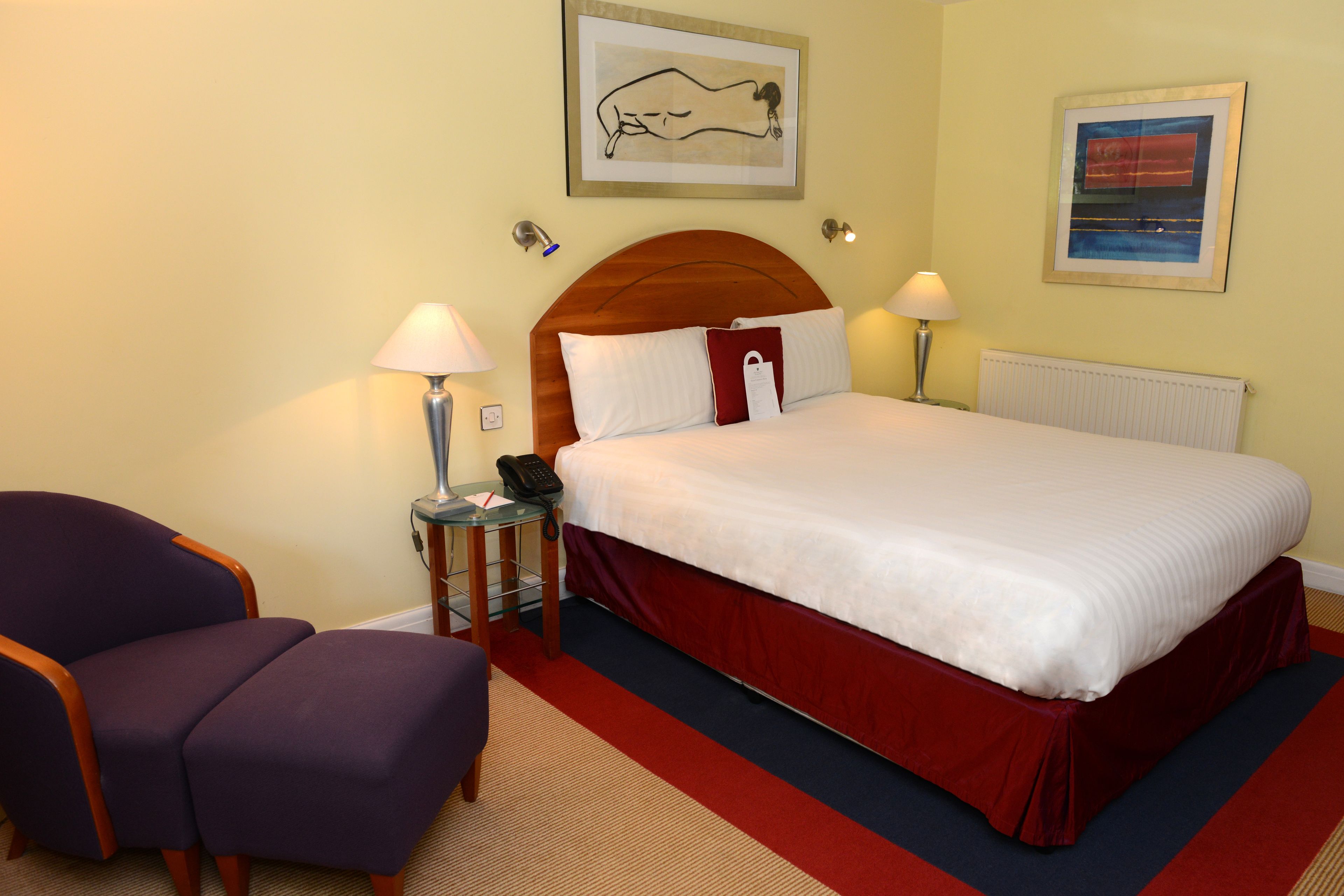 A hotel room with a bed, two chairs, a nightstand, and a lamp.