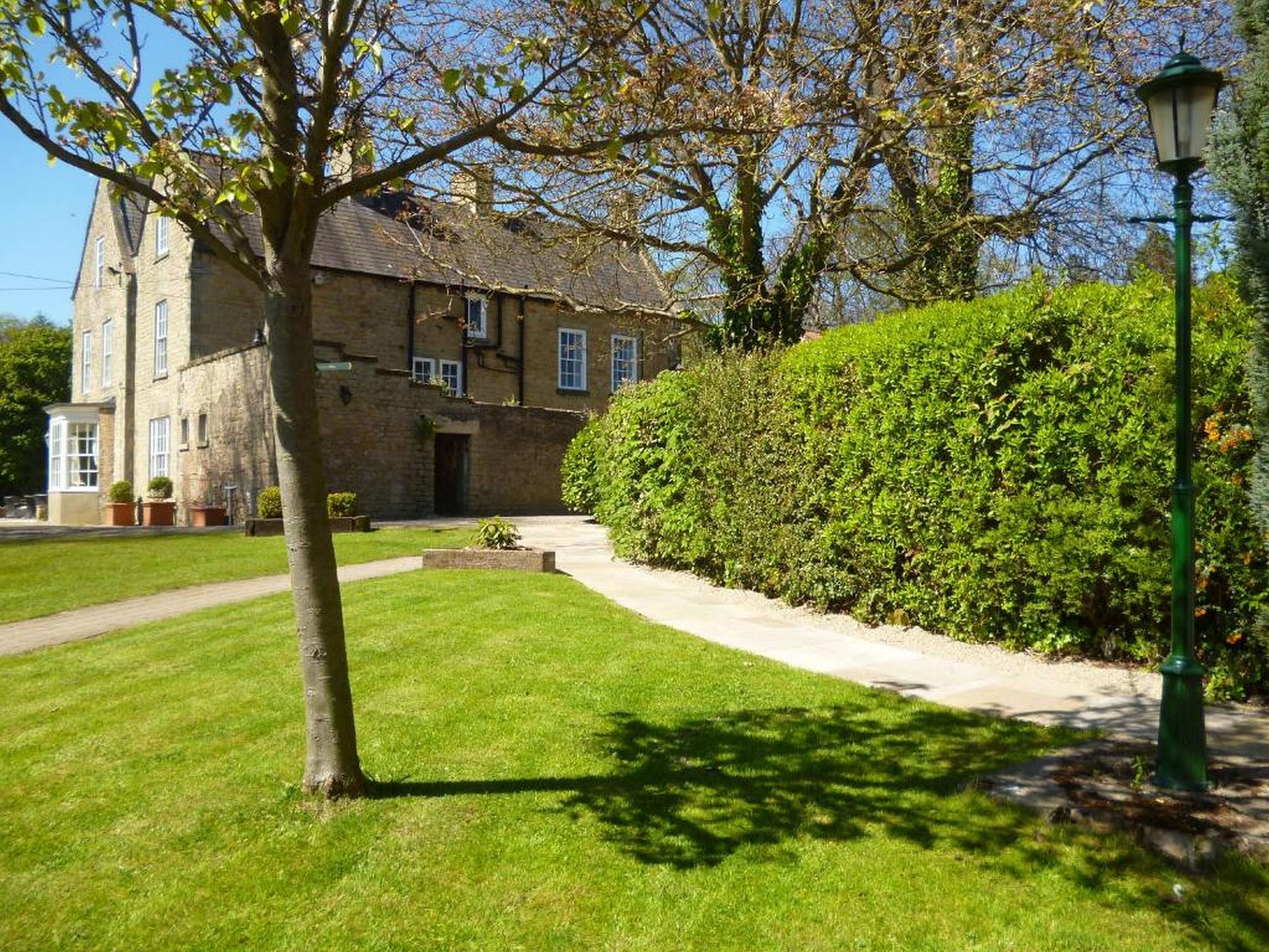 A stone building with a large lawn and a hedge.