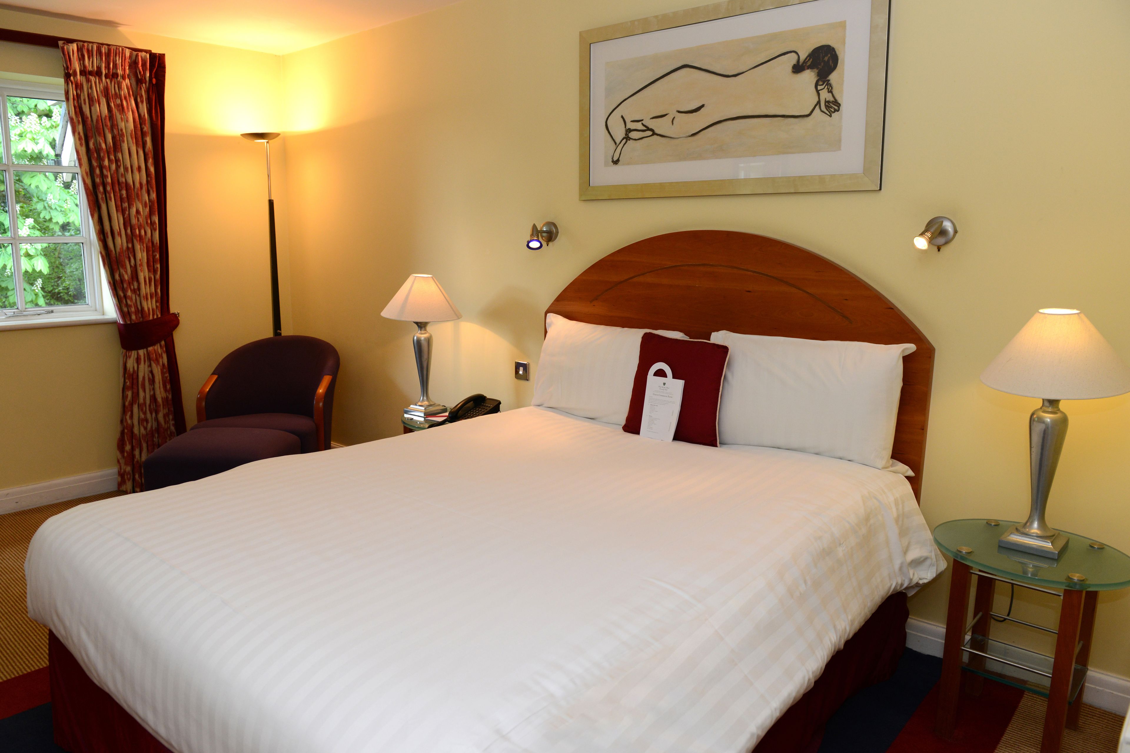 Une chambre d’hôtel avec un grand lit, deux lampes de chevet, une chaise, une petite table et une fenêtre avec des rideaux.